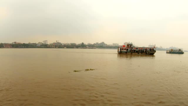 zwei-Fähren-schwimmen-auf-dem-voll-fließenden-Fluss-Hoogli-Gebäude-der-Stadt-Kalkutta-am-Ufer