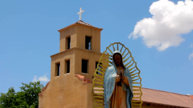 Estatua-de-la-Virgen-de-Guadalupe-que-pacíficamente-frente-a-una-iglesia-de-Adobe