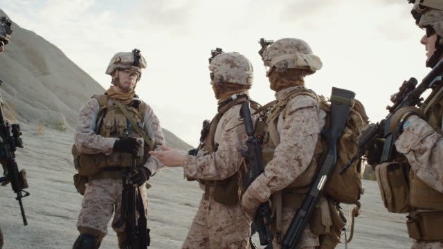 Gruppe-von-Soldaten-steht-in-einem-Kreis-und-hört-Aufträge-von-Commander-während-Briefing-vor-der-militärischen-Operation-in-der-Wüste.-zeitlupe.