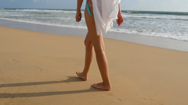 Weiblichen-Fuß-auf-Sand-mit-Meer-Wellen-Hintergrund-treten.-Schöne-Frau-im-Badeanzug-und-Hemd-zu-Fuß-am-Strand-barfuß.-Junge-Mädchen-geht-direkt-am-Meer.-Sommer-Urlaub-Konzept.-Nahaufnahme