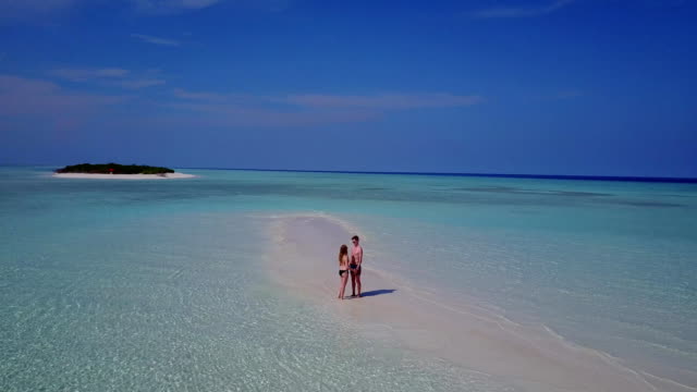 v03866-Aerial-flying-drone-view-of-Maldives-white-sandy-beach-2-people-young-couple-man-woman-romantic-love-on-sunny-tropical-paradise-island-with-aqua-blue-sky-sea-water-ocean-4k