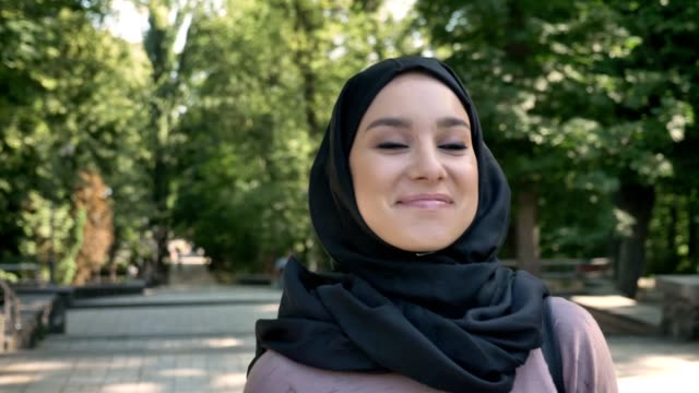 Muslimische-Mädchen-glückliches-ist-im-Park-tagsüber-im-Sommer-Fuß-lächelnd,-beobachten,-religiöse-Konzept