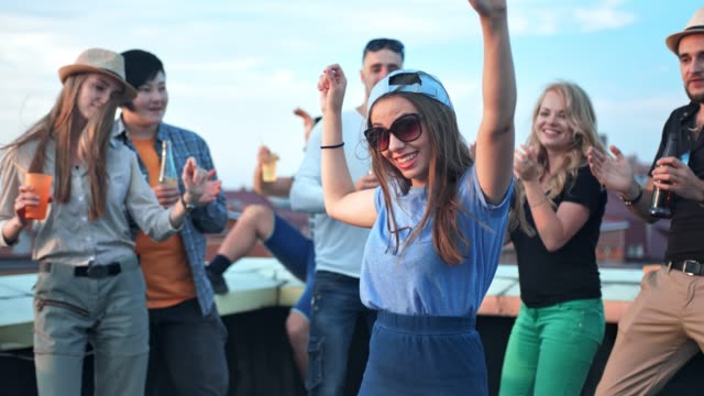 Young-woman-dancing-in-the-middle-of-crowds-with-raising-arms-at-rooftop-party