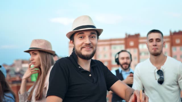 Pretty-brutal-Caucasian-man-in-hat-surrounded-by-friends-dancing-and-having-fun-at-rooftop-party