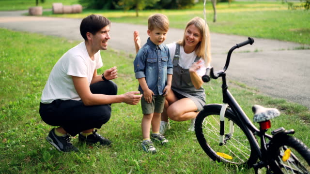 Loving-parents-are-making-surprise-for-little-son-closing-his-eyes-and-giving-him-new-bicycle-as-present,-happy-boy-is-looking-at-bike-and-talking-to-mother-and-father.
