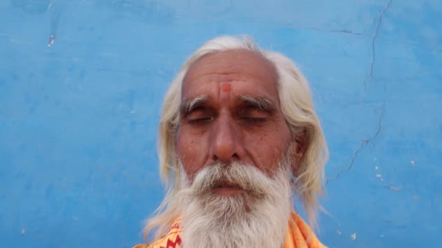 Sadhu,-Hindu-Heilige-sitzt-vor-einem-Tempel-in-der-Meditation-vor-einer-blauen-Wand