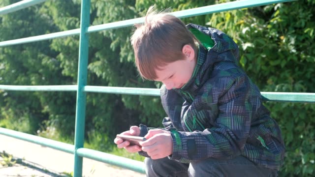 El-niño-juega-un-juego-en-su-teléfono-móvil-mientras-está-sentado-en-el-parque.