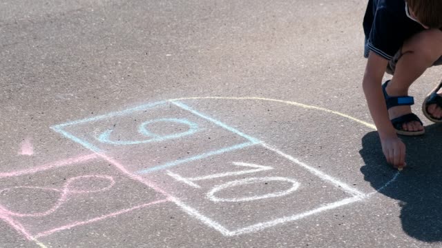 Boy-is-drawing-hopscotch-on-the-asphalt.-Painting-a-sun.
