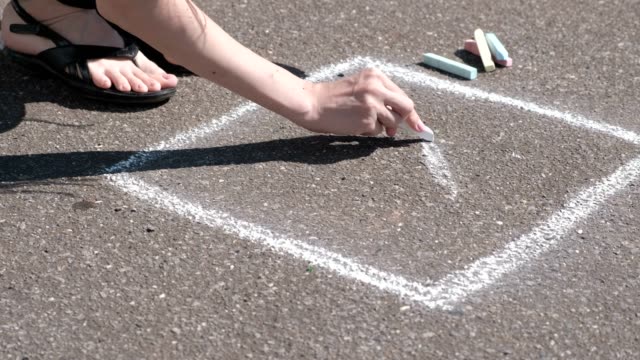 Woman-draws-a-hopscotch-on-the-asphalt-with-white-chalk.-Close-up-hands.