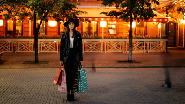 Time-Lapse-junge-Frau-Shopaholic-stehen-draußen-auf-der-Straße-mit-Einkaufstüten-und-Blick-in-die-Kamera-während-der-Zustrom-von-Menschen-bewegt-um-sie-herum.