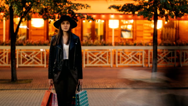Time-lapse-portrait-of-tired-female-shopper-beautiful-woman-standing-with-paper-bags-in-the-street-and-looking-at-camera-while-people-are-moving-around-in-hurry.