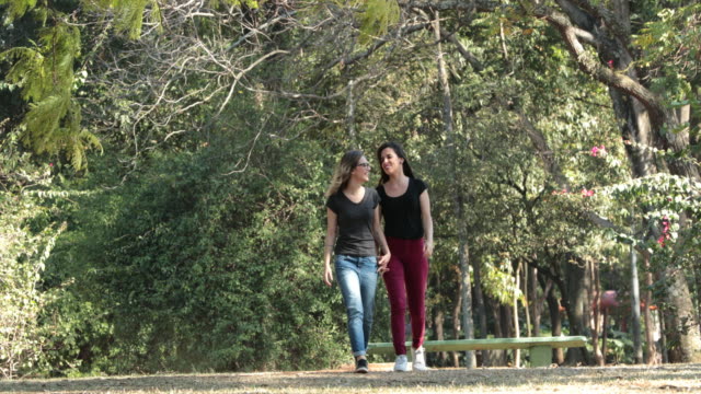 Two-girlfriends-together-walking-at-the-park-embracing-each-other-laughing