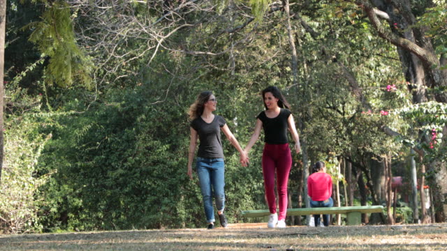 Zwei-Freundinnen-zusammen-zu-Fuß-in-den-Park,-die-Hand-in-Hand