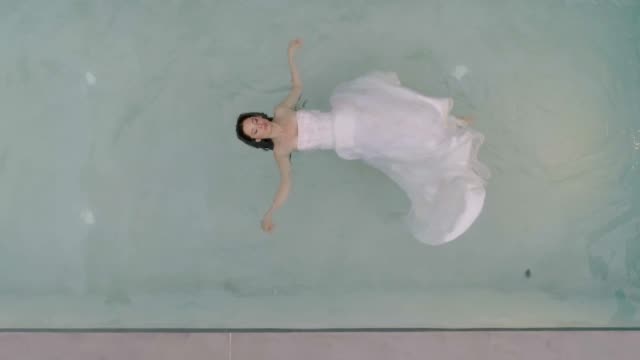 Luftaufnahme-einer-Frau,-die-mit-einem-Hochzeitskleid-im-Wasser-schwimmt,-Griechenland.