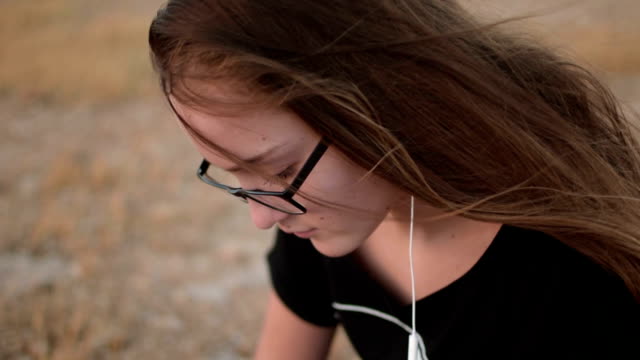 Teenage-girl-with-eyeglasses-sitting-on-the-ground-and-listening-to-the-music,-close-up