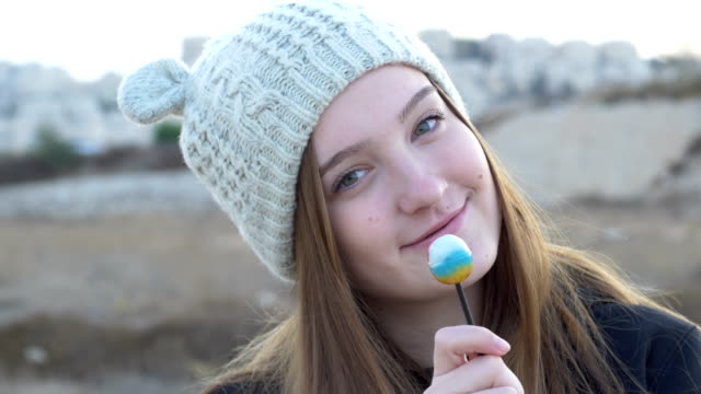 Schöne-Teenager-Mädchen-in-einer-grauen-Strickmütze,-die-zeigen-und-essen-Lollipop,-künstlerisches-und-ausdrucksstarkes-Spiel-unter-der-Kamera,-Stock-Footage.