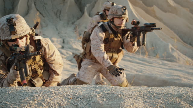 Grupo-de-soldados-Acuéstese-en-la-colina,-apunte-a-través-del-alcance-del-rifle-de-asalto-en-medio-del-desierto.-Cámara-lenta.