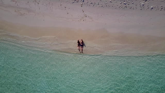 v03929-Aerial-flying-drone-view-of-Maldives-white-sandy-beach-2-people-young-couple-man-woman-romantic-love-on-sunny-tropical-paradise-island-with-aqua-blue-sky-sea-water-ocean-4k