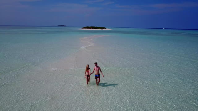 v04000-Aerial-flying-drone-view-of-Maldives-white-sandy-beach-2-people-young-couple-man-woman-romantic-love-on-sunny-tropical-paradise-island-with-aqua-blue-sky-sea-water-ocean-4k