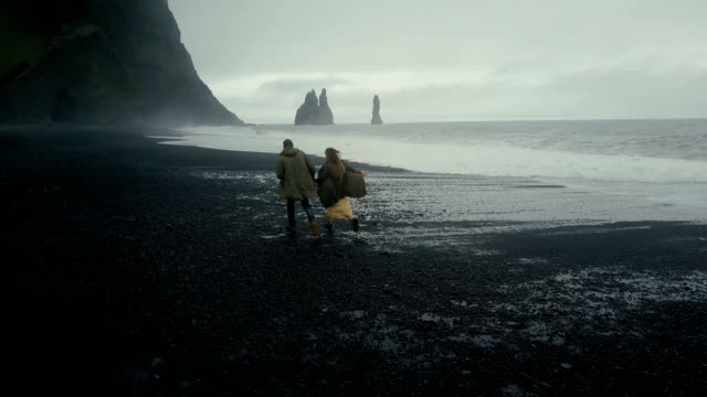 Luftaufnahme-der-junge-Hipster-paar,-die-auf-der-schwarzen-vulkanischen-Strand-in-der-Nähe-der-Troll-Zehen-in-Island-zurück