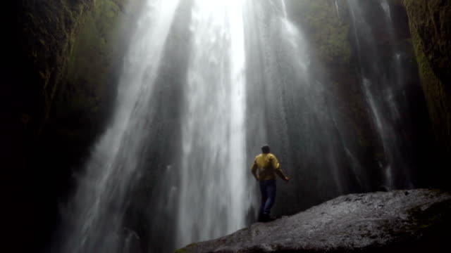 Junger-Reisender-Mann-zu-Fuß-in-der-Nähe-des-mächtigen-Gljufrabui-Wasserfalls-in-Island.-Männliche-Freude-springen-und-glücklich