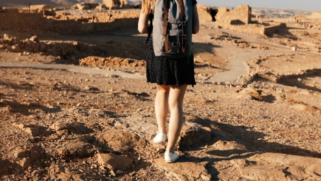 Frau-mit-Rucksack-erkundet-Wüste-Ruinen.-Schöne-europäische-touristische-Spaziergänge-auf-Felsen-und-Sand.-Masada-Israel-4K