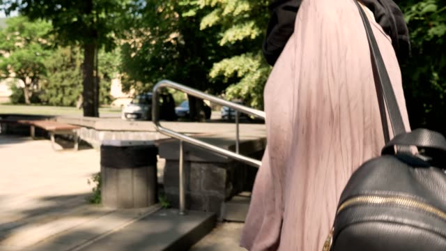 Young-attractive-muslim-girl-in-hijab-walks-up-stairs-in-park-in-daytime-in-summer,-smiling,-crossing-street,-religious-concept,-urban-concept,-side-view