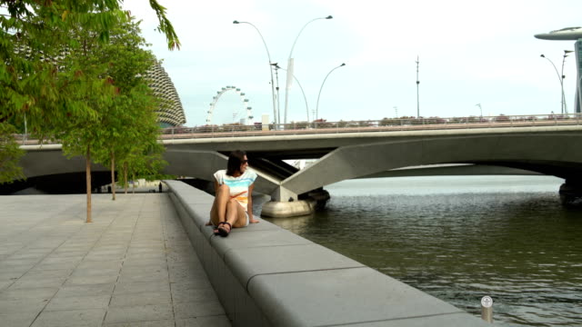 Eine-Frau-sitzt-auf-einer-Brüstung-am-Ufer-des-Flusses