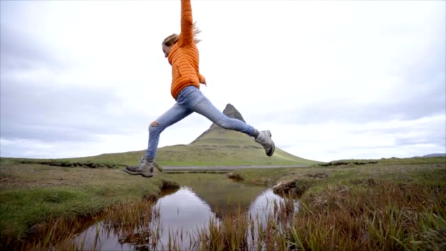 Mujer-joven-en-Islandia-saltando-sobre-Río-fiordo-en-la-famosa-montaña-de-Kirkjufell