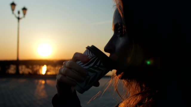 profile-view-of-girl-sipping-drink-from-cardboard-cup-in-evening-on-a-city-quay