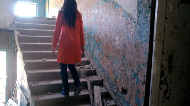 Frau-in-einem-roten-Mantel-inspiziert-zerstörten-Gebäude-nach-der-Katastrophe-Erdbeben,-Flut,-Feuer.-Gehe-die-Treppe-hoch.