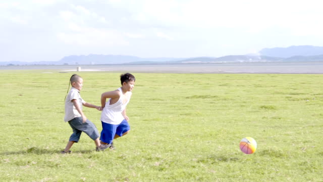 Dos-muchachos-asiáticos-jugando-al-fútbol,-diversión,-feliz.-El-fondo-de-la-pradera-rural.-Video-4K-lenta