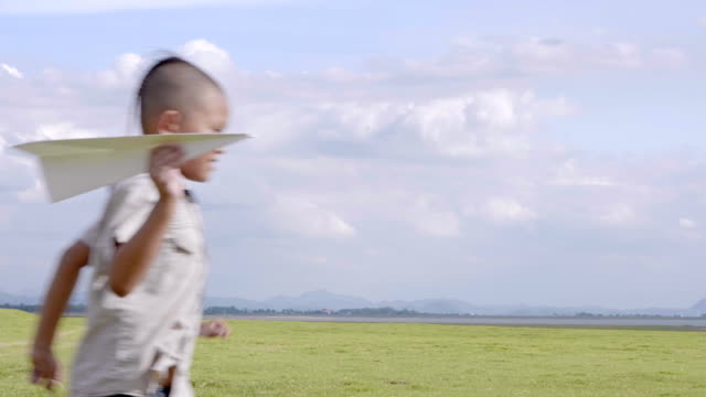 Kleiner-Junge-zwei-alte-7-Jahre-glücklich-mit-einen-laufen-und-werfen-Papierflieger-auf-Wiese-im-Sommer-in-der-Natur-Sonnenuntergang-Zeit.-4K-Video-Zeitlupe
