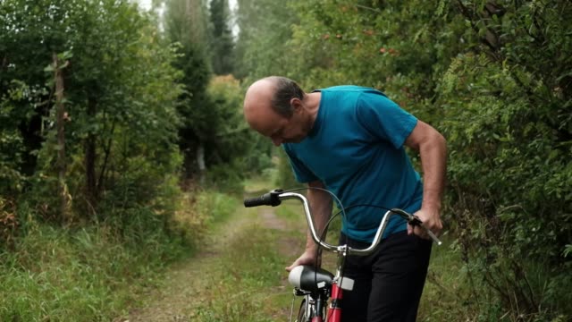 Senior-kaukasischen-Männchen-im-blauen-T-shirt-versucht,-ein-Fahrrad-zu-fahren.