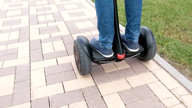 Person's-legs-in-sneakers-rolling-on-gyro-scooter-on-paving-road.