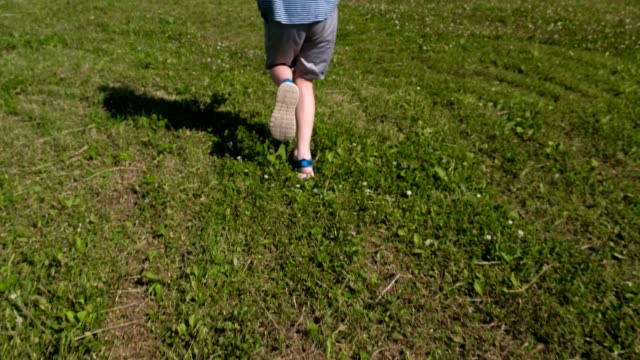 Boy-runs-fast-on-the-green-grass,-close-up-legs-in-sandals.