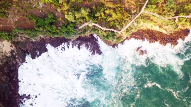 4K-top-down-aerial-drone-of-crashing-waves-on-cliff-and-long-wooden-platform-at-Timang-beach.