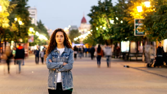 Time-lapse-portrait-of-lonely-young-lady-standing-in-street-downtown-with-arms-crossed-while-crowds-of-men-and-women-are-passing-by.-Loneliness-and-time-concept.