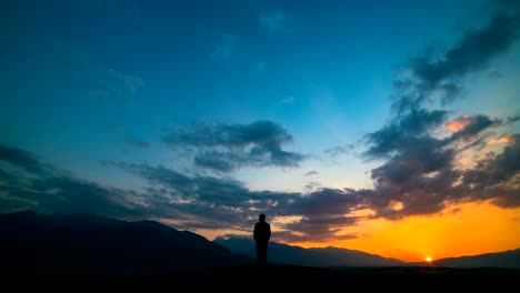 The-man-standing-on-a-mountain-against-a-sunset-with-northern-light.-time-lapse