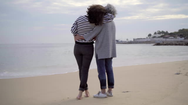Happy-senior-mother-and-adult-daughter-hugging-on-sandy-beach.