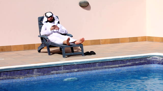 saudi-arabischer-Mann-mit-seinem-Handy-am-Swimmingpool