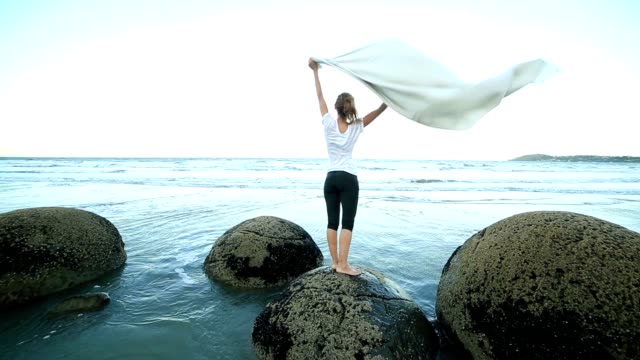 One-female-stands-on-boulder,-holds-blanket-in-the-air