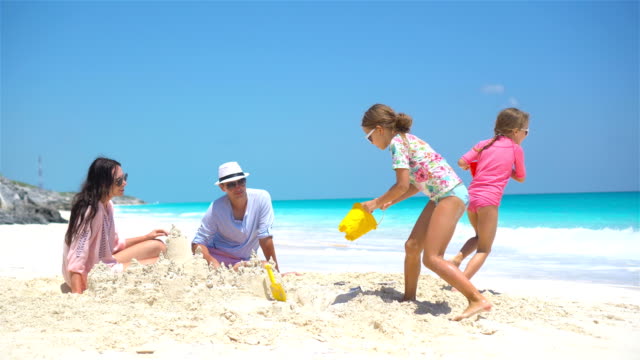 Familia-con-dos-niños-haciendo-castillos-de-arena-en-la-playa-tropical