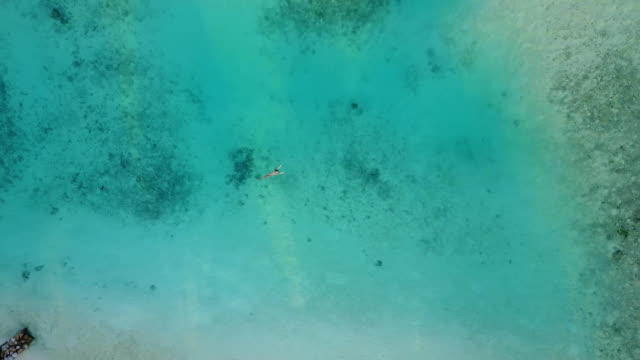 Cámara-aérea-es-ascendente-sobre-una-mujer-atractiva-en-bikini-flotando-en-las-aguas-cristalinas-del-mar-en-el-atolón-tropical-island-resort.-Muy-sexy-chica-nadando-en-el-Océano-Índico
