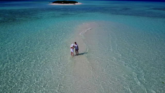 v03952-Aerial-flying-drone-view-of-Maldives-white-sandy-beach-2-people-young-couple-man-woman-romantic-love-on-sunny-tropical-paradise-island-with-aqua-blue-sky-sea-water-ocean-4k
