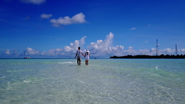 v03949-Aerial-flying-drone-view-of-Maldives-white-sandy-beach-2-people-young-couple-man-woman-romantic-love-on-sunny-tropical-paradise-island-with-aqua-blue-sky-sea-water-ocean-4k