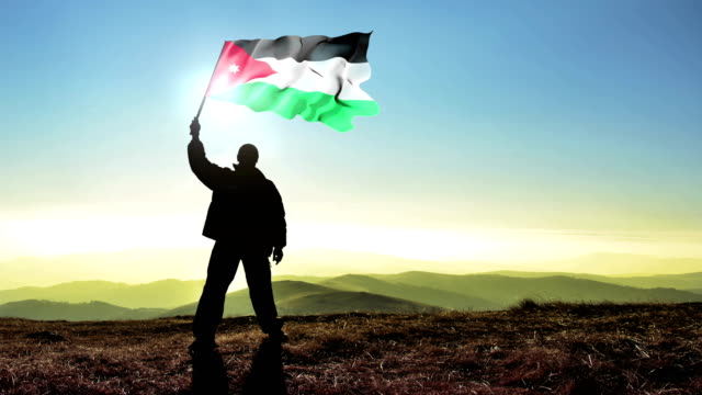 Ganador-de-hombre-exitoso-silueta-ondeando-la-bandera-de-Jordania-en-la-parte-superior-del-pico-de-la-montaña,-fondo-Cinemagraph-lazo