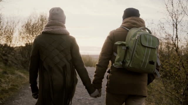 Back-view-of-young-couple-walking-together-in-national-nature-park.-Man-and-woman-holding-hands-and-talking