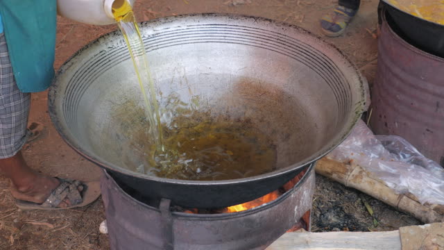 Woman-pouring-fried-oil-into-a-large-outdoor-wok-cooking-to-deep-fry-chicken
