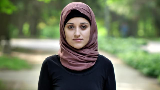 Retrato-de-una-joven-muchacha-triste-en-hijab,-al-aire-libre,-en-un-parque-en-el-fondo.-50-fps